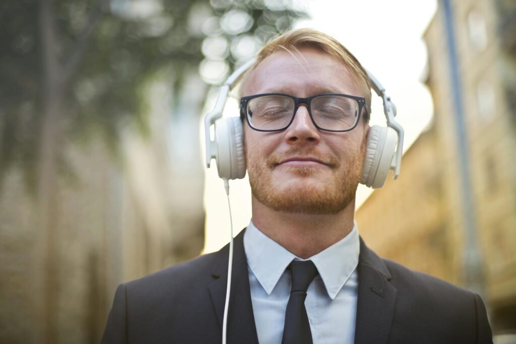 Portrait of a young man in a suit, wearing headphones and enjoying music outdoors with a blurred urban background.