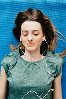 Young woman lying on yoga mat with earphones, eyes closed in relaxation.