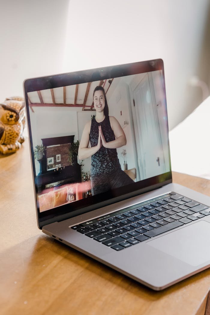 A woman participates in a virtual yoga class from home using a laptop.