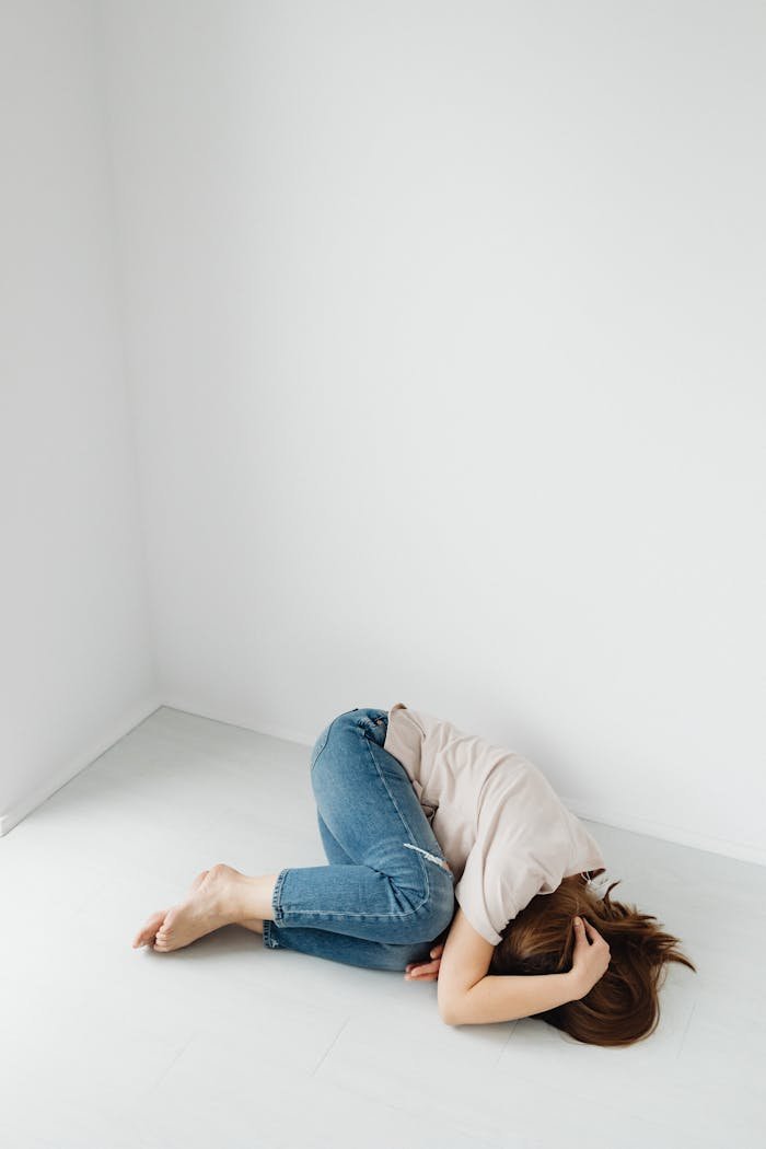 A woman lies curled up on the floor in an empty white room, conveying introspection.