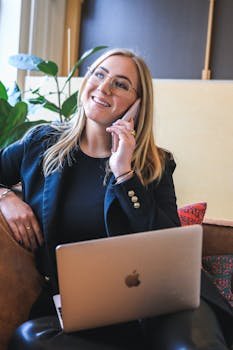 pexels-photo-5839459-5839459 Confident young professional woman working remotely on phone call, utilizing laptop in modern setting.