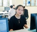 A young woman sits at a desk in a computer lab, smiling into the camera.